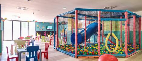 A play area with a ball pit and slides, surrounded by tables and chairs.