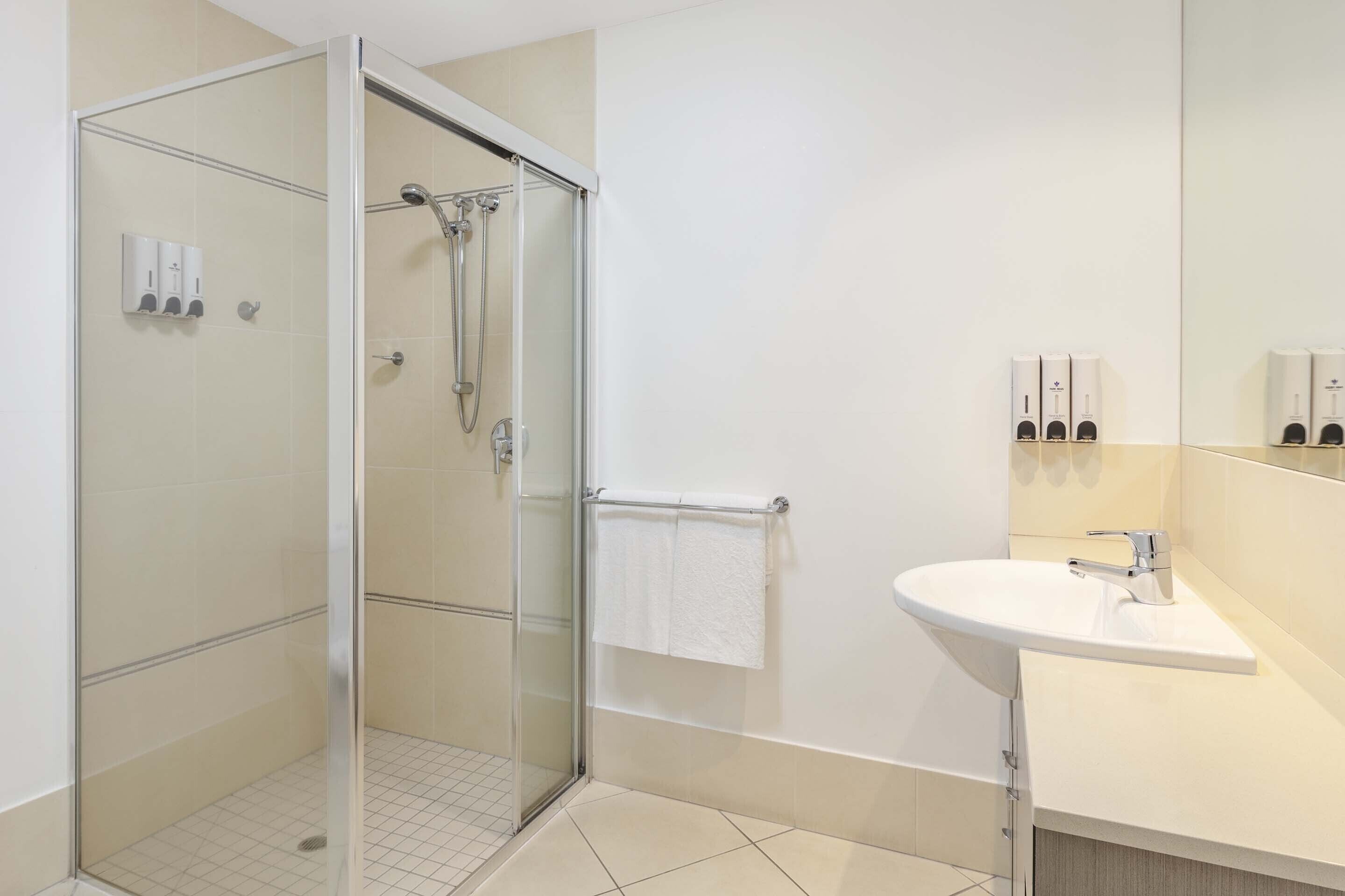 Un baño moderno con ducha de vidrio, lavamanos blanco y un perchero para toallas.