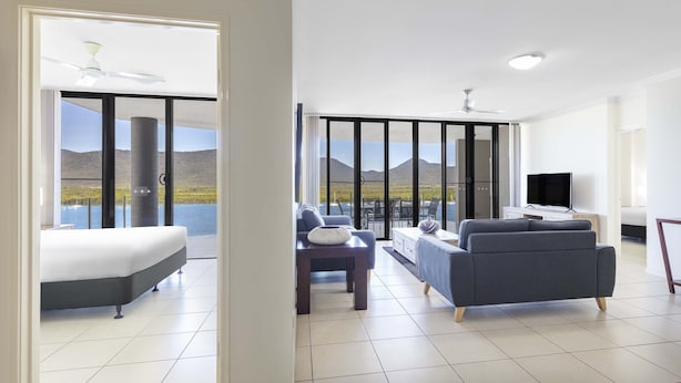 Een ruime woonkamer met een balkon, een bed, een slaapbank en een televisie.