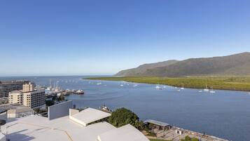 A marina with boats, a building with a flat roof, and a hilly landscape in the background.