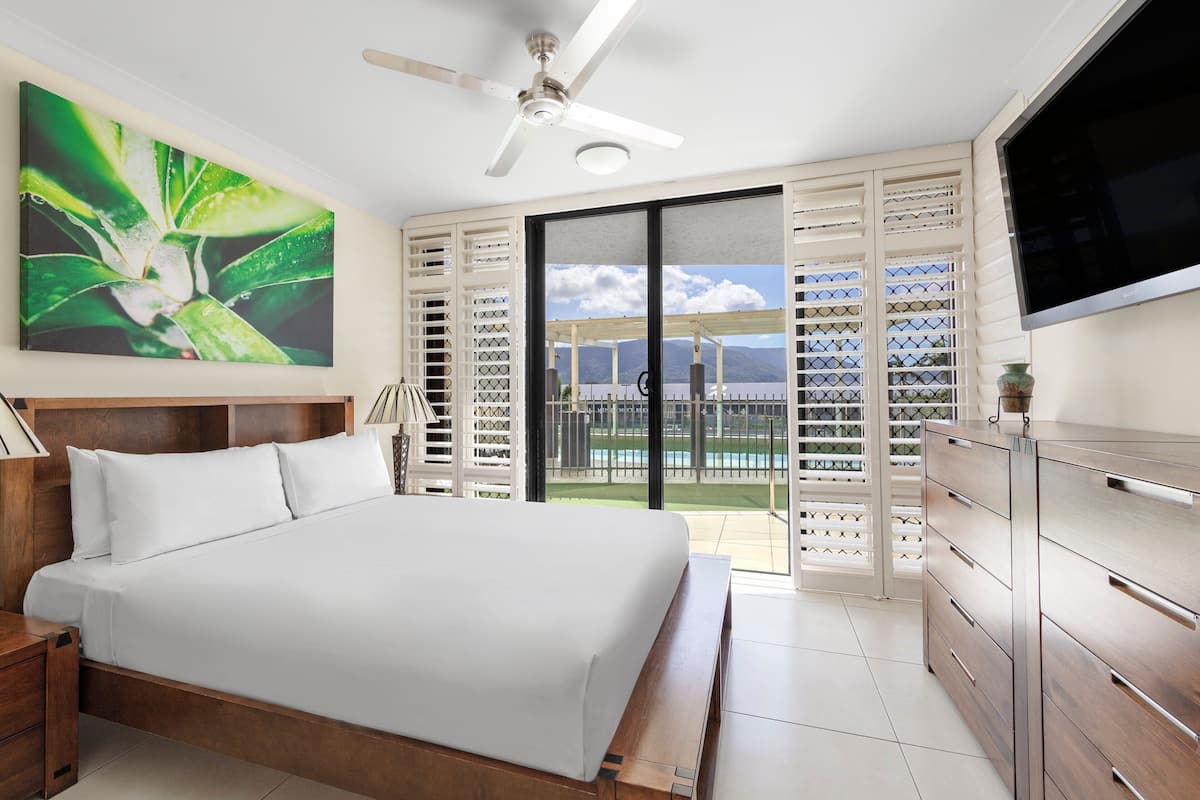 A bedroom with a bed, a TV, and a balcony with a view of the mountains.