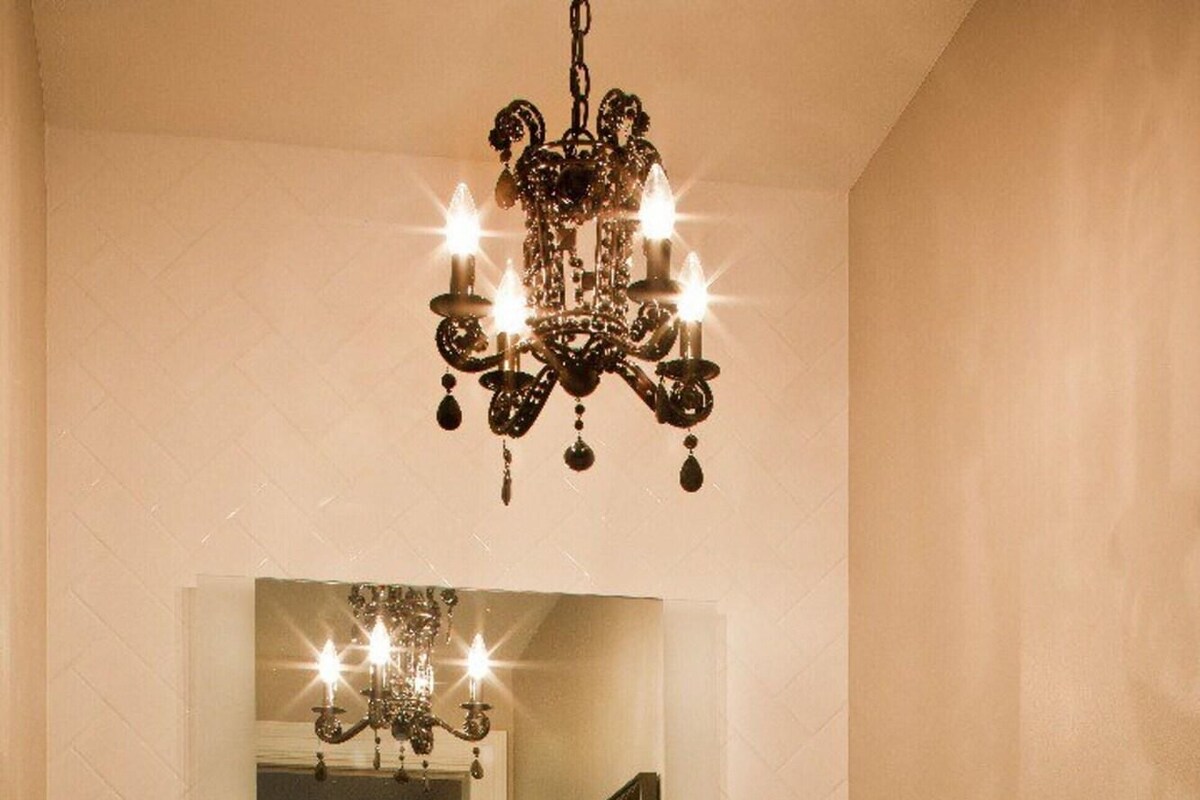 A bathroom with a large mirror, a chandelier, a sink with a towel, and a potted orchid.