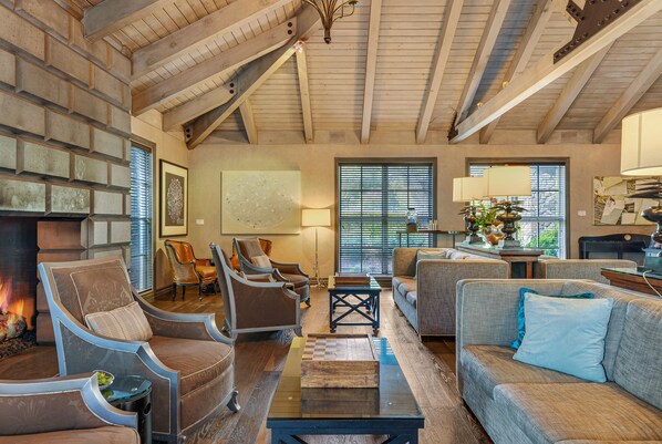 A spacious living room with a fireplace, comfortable seating, and a high ceiling with exposed beams.