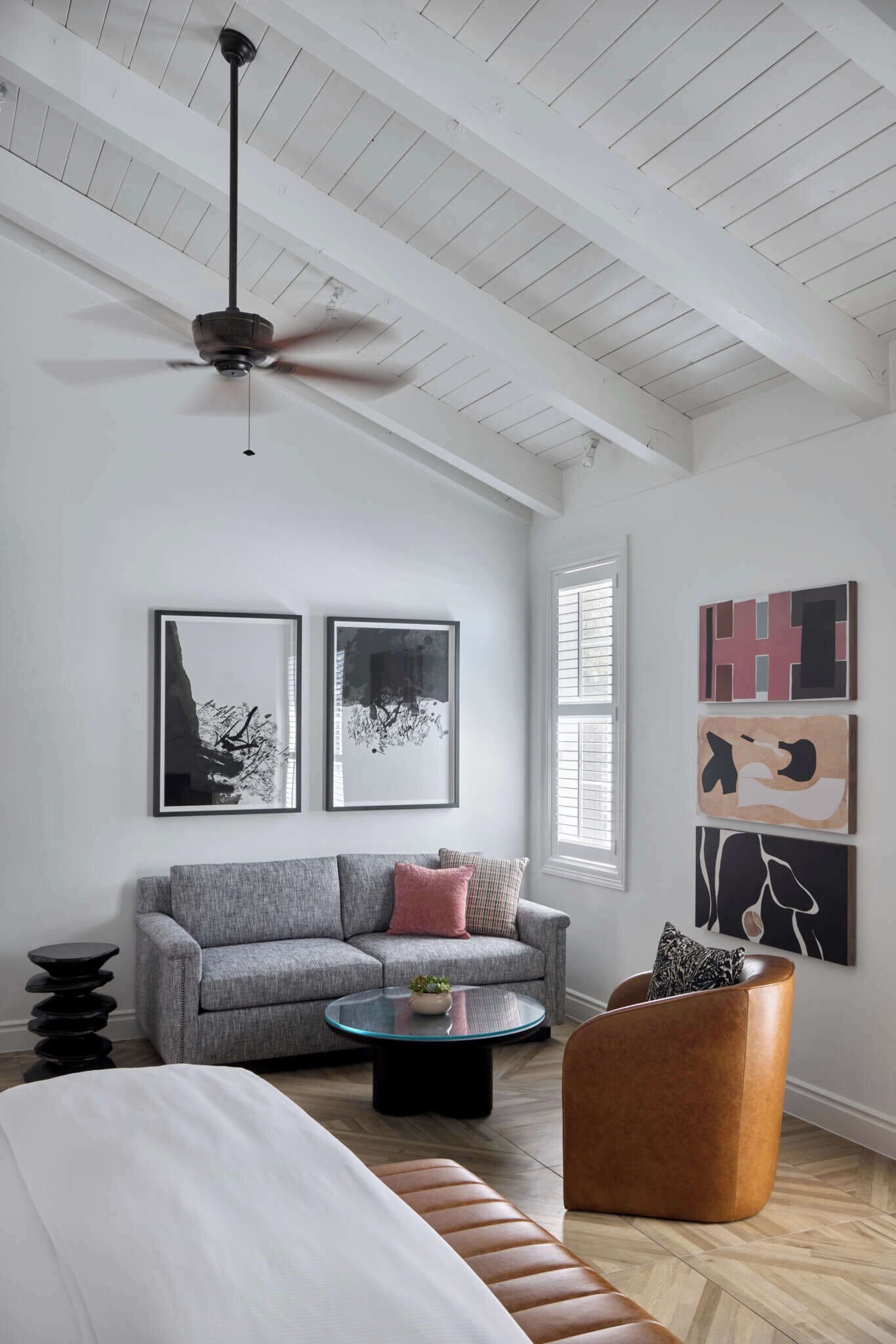 Una sala de estar moderna con techo alto, ventilador de techo, sofá gris, mesa de centro redonda y sillón marrón.