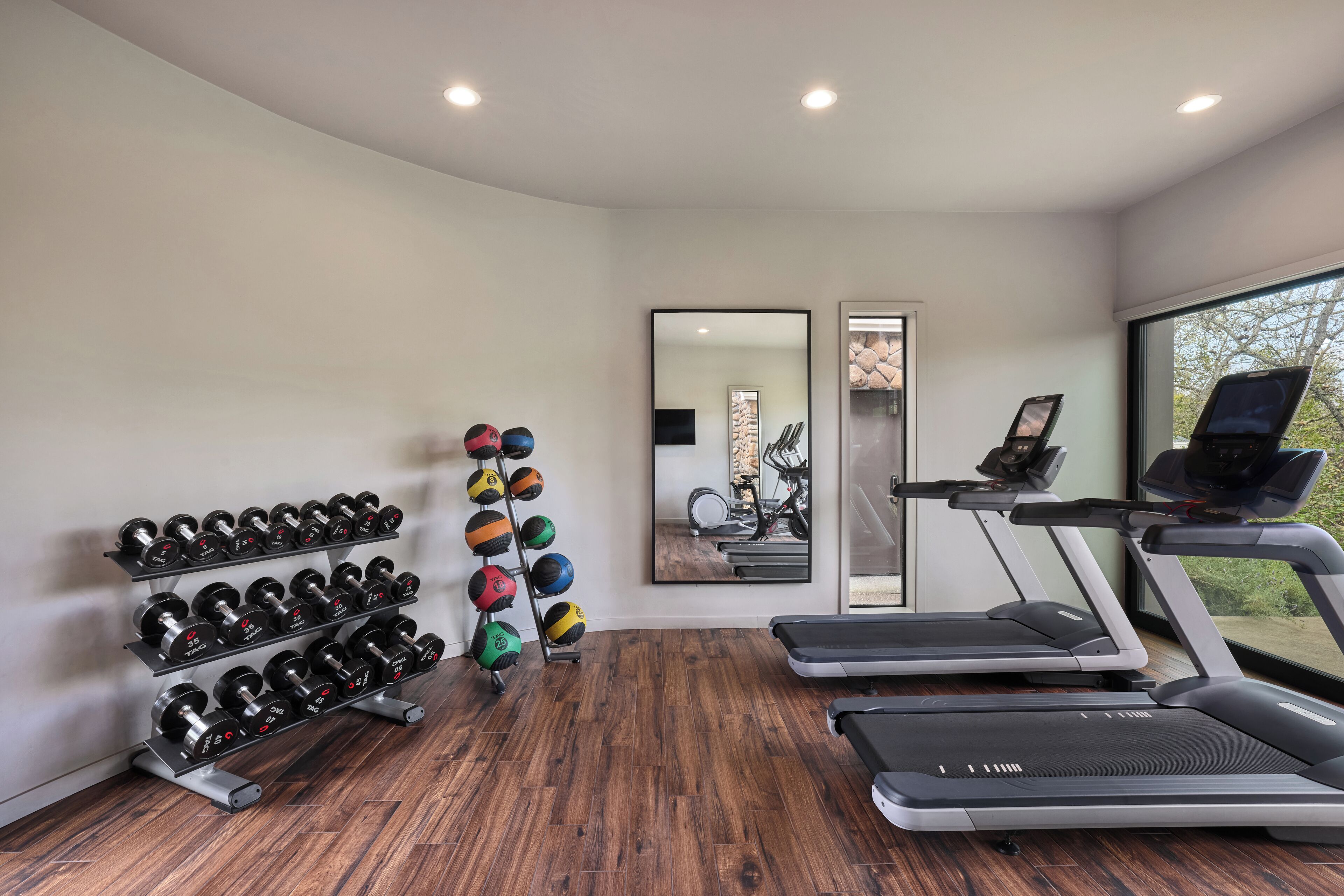 A modern gym with treadmills, a mirror, and a rack of dumbbells.