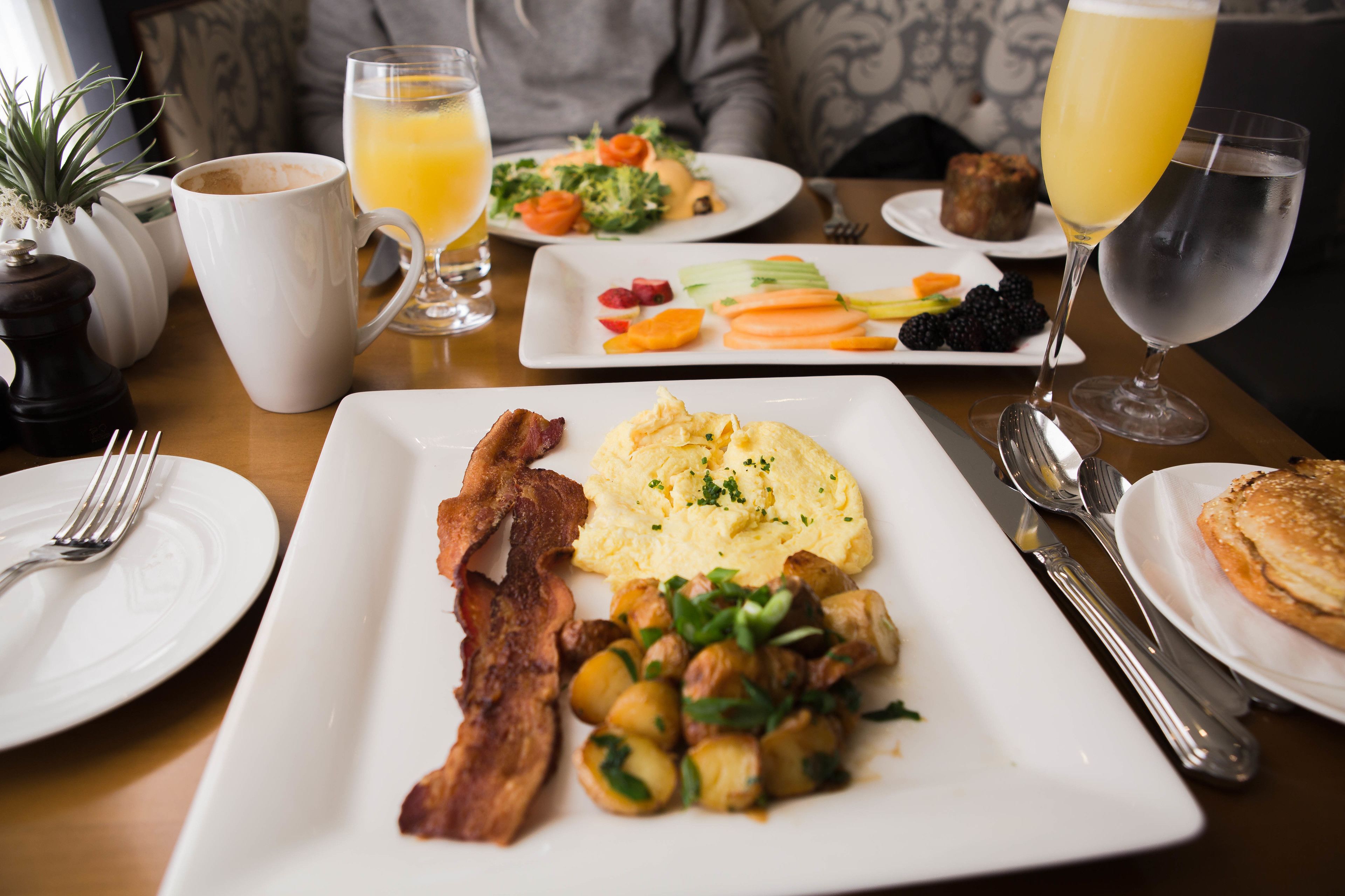 A breakfast setting with plates of eggs, bacon, and vegetables, a glass of orange juice, and a glass of water.