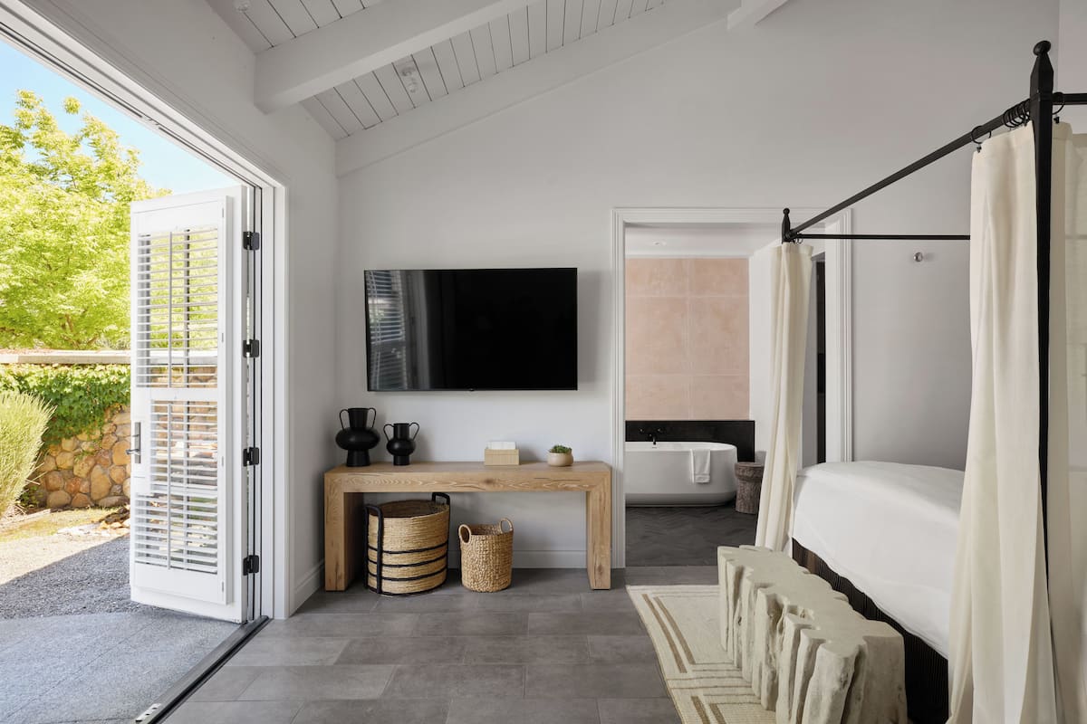 A modern bedroom with a bed, a TV, a bathtub, and a wooden bench.