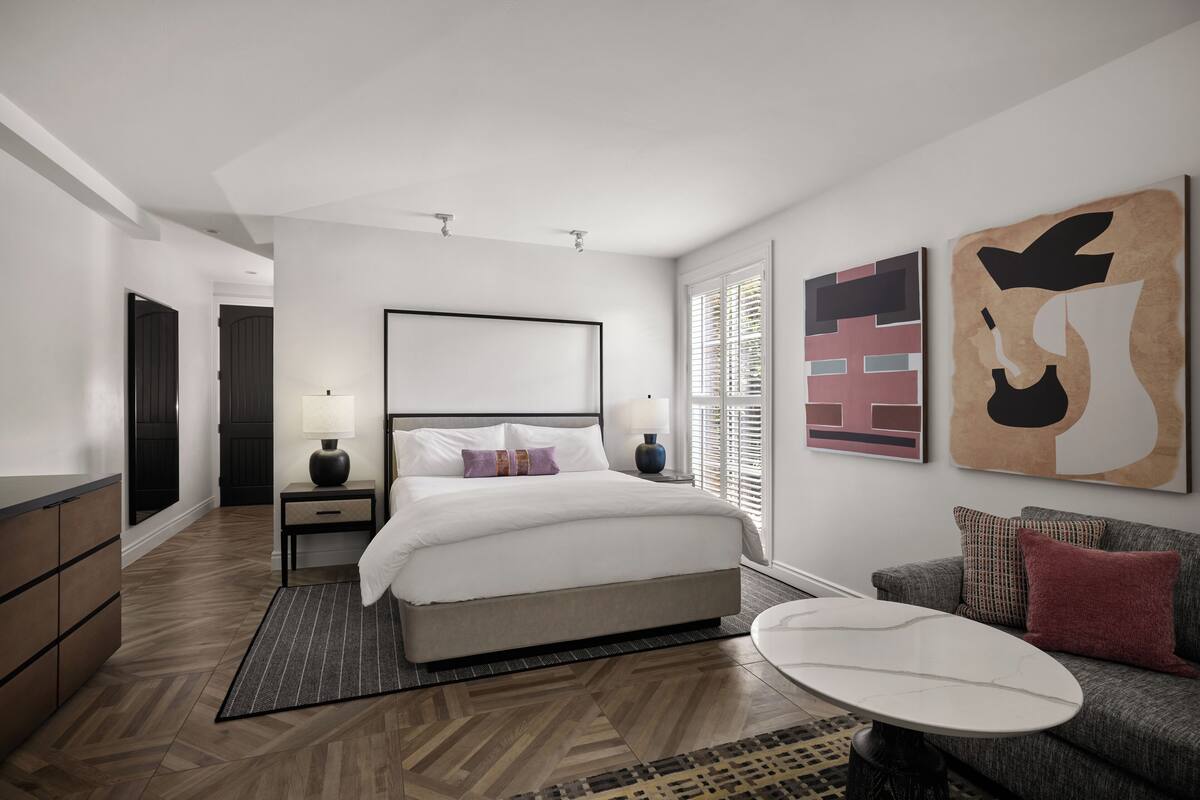 A modern hotel room with a large bed, bedside tables, a sofa, and artwork on the walls.