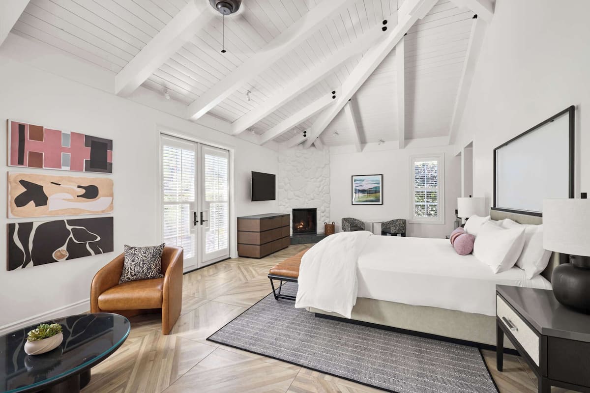 A modern bedroom with a large bed, a seating area with a chair, a TV, and artwork on the walls.