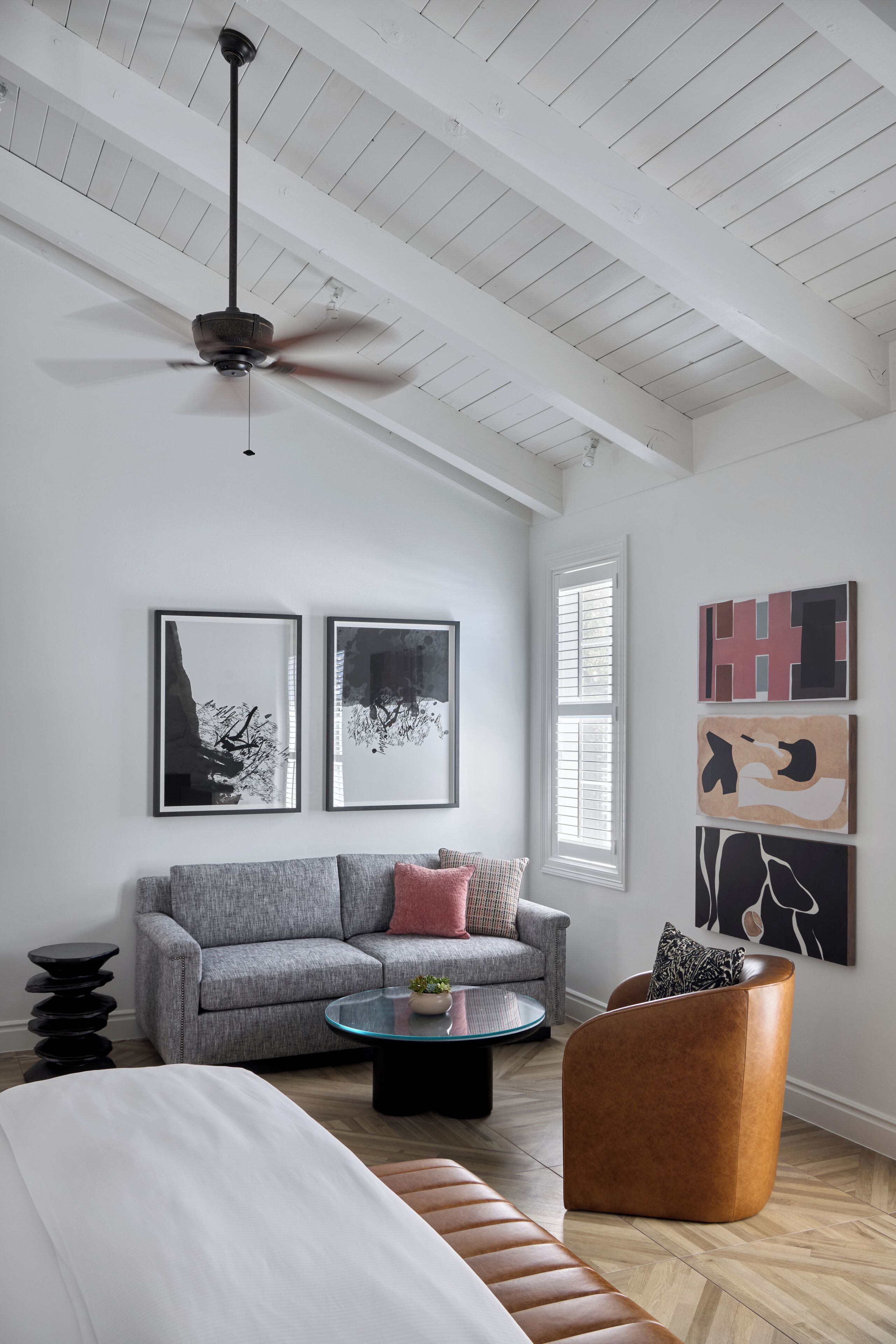 A modern living room with a high ceiling, a ceiling fan, a grey sofa, a round coffee table, and a brown armchair.