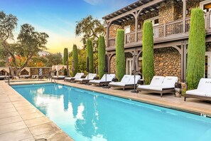 Zona junto a la piscina con sillones de descanso y un edificio de piedra con balcón.