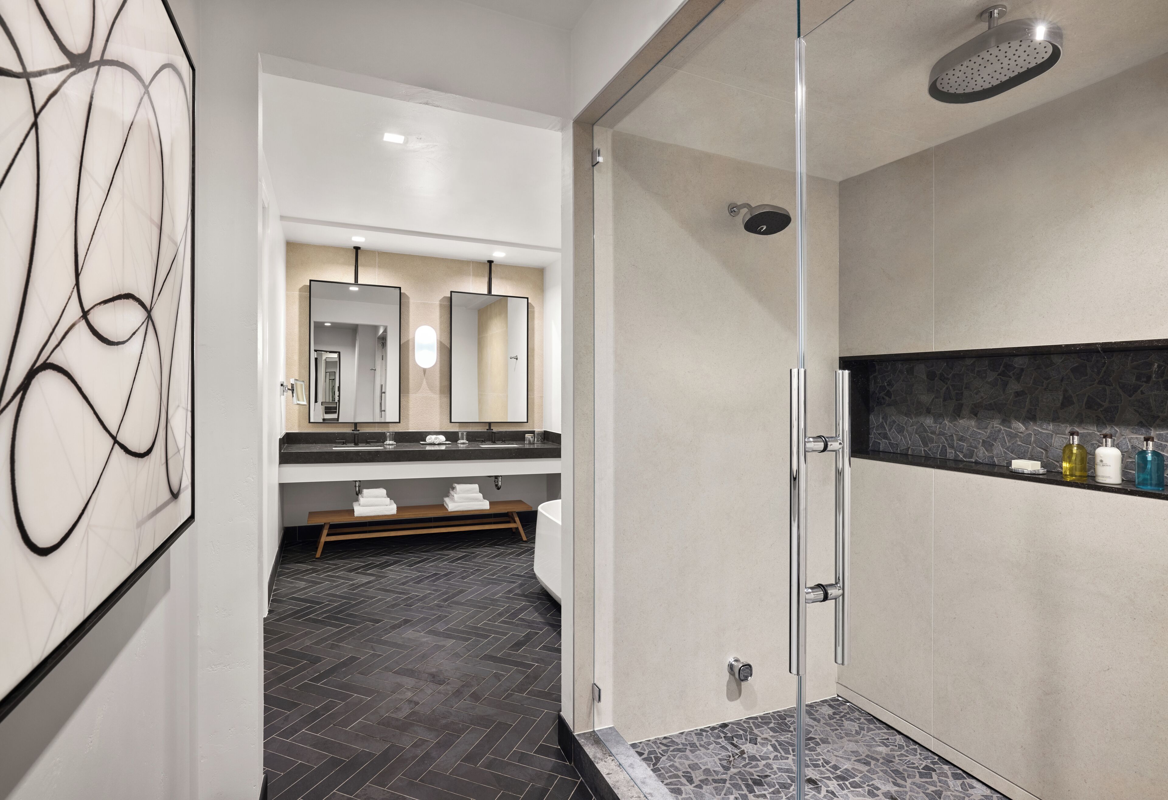 A modern bathroom with a glass-enclosed shower, a large mirror, and a dark tiled floor.