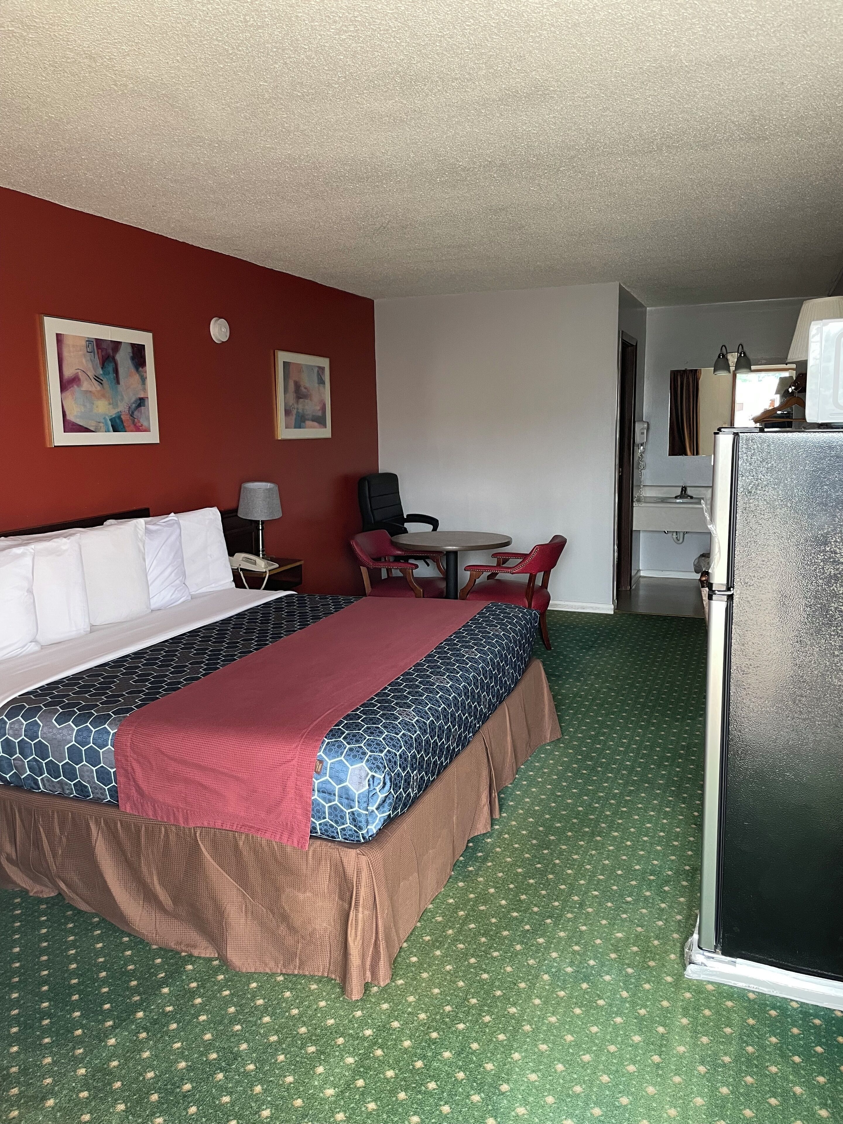 Une chambre d’hôtel avec un lit, un bureau, une chaise, un réfrigérateur et deux tableaux accrochés au mur.