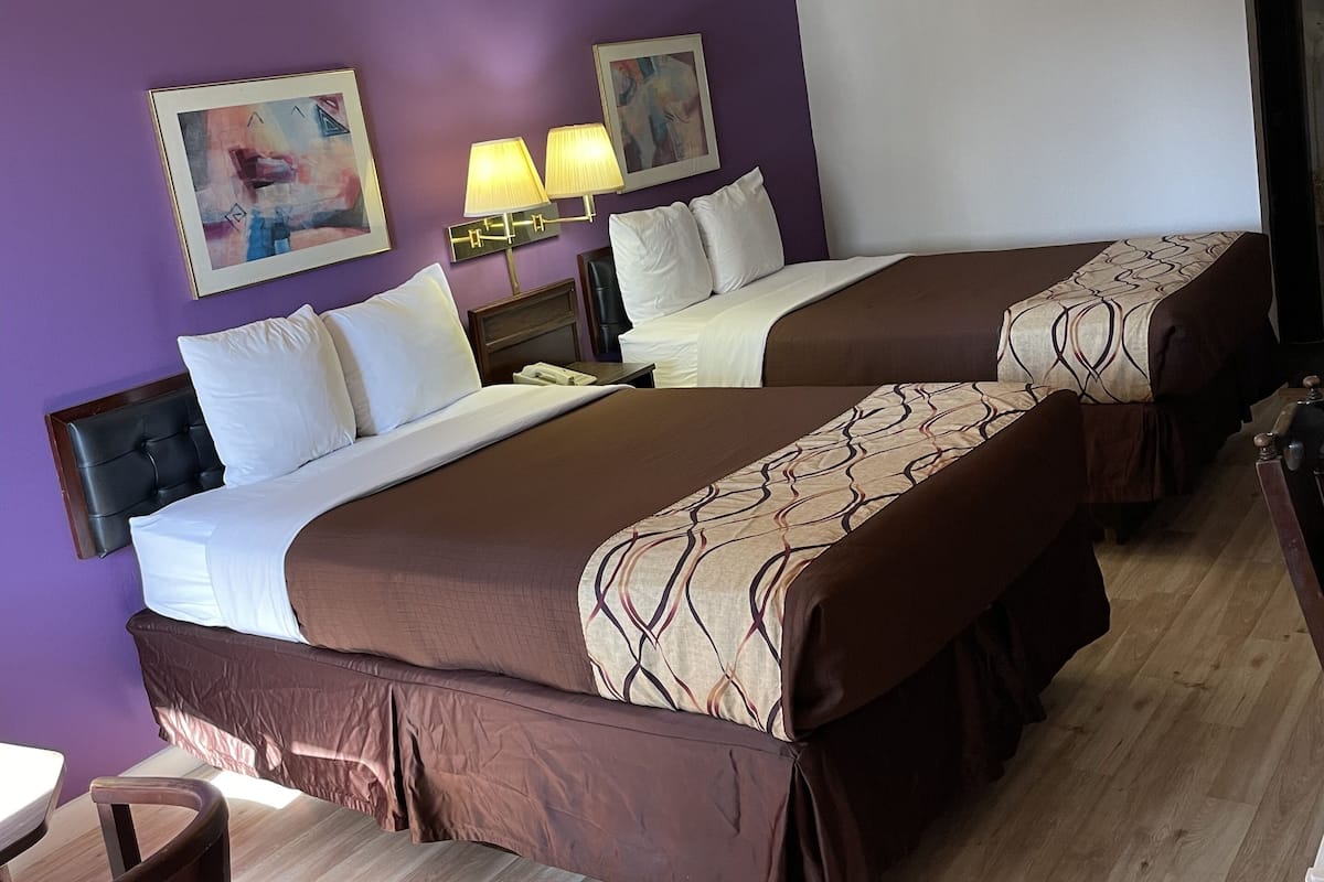 Habitación de hotel con dos camas, paredes moradas, suelo de madera y obras de arte.