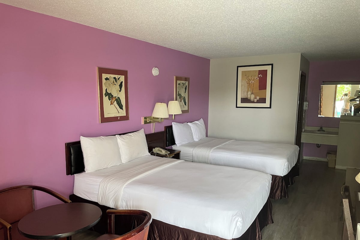 Habitación de hotel con dos camas, un escritorio y una silla. Hay lámparas de pared y cuadros enmarcados.
