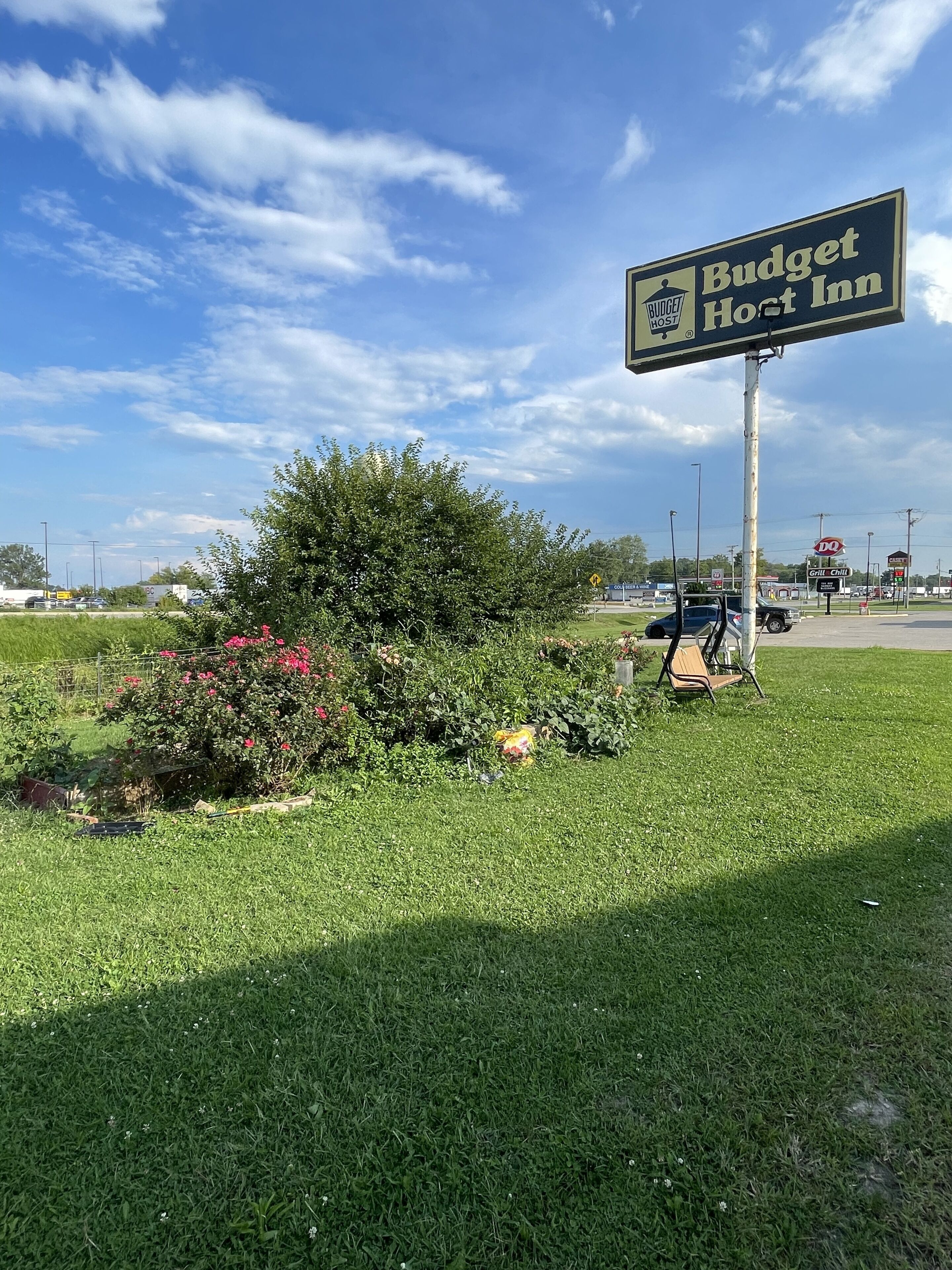 A sign for Budget Host Inn with a grassy area and a bush in the foreground.