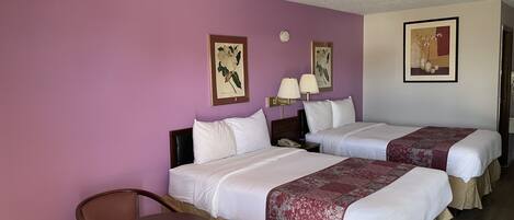 A hotel room with two beds, a small table, and chairs. There are wall-mounted lamps and framed pictures on the walls.