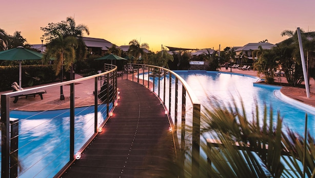 A pool area with a wooden walkway, lounge chairs, and umbrellas.