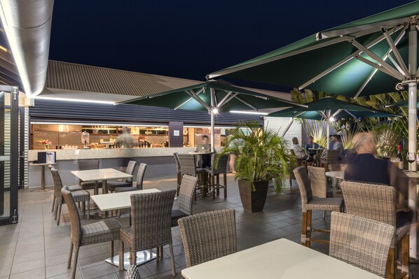 An outdoor dining area with wicker furniture and green umbrellas. - Oaks Cable Beach Resort (Cable Beach)
