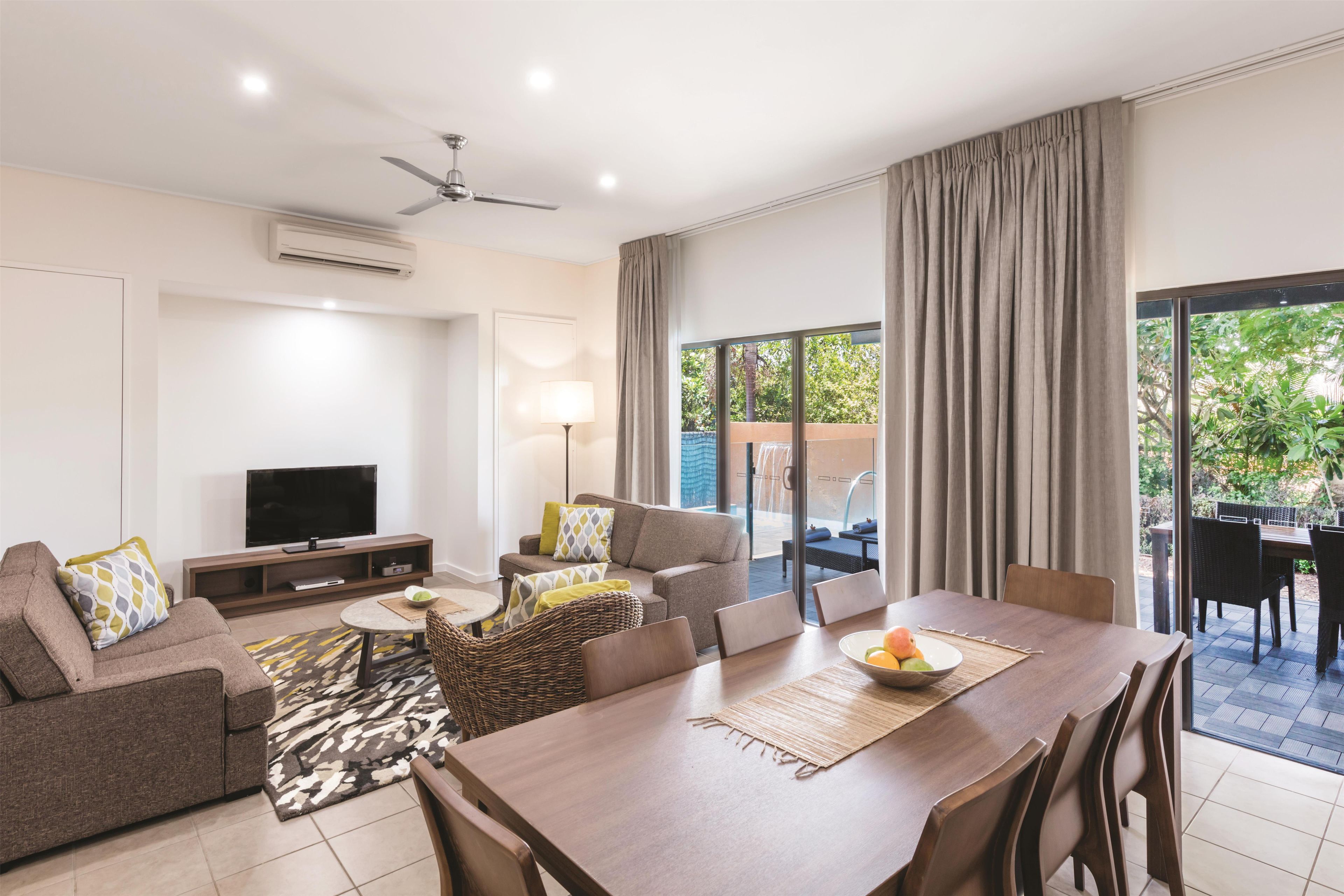 A modern living room with a flat-screen TV, sofa, dining table, and a ceiling fan.