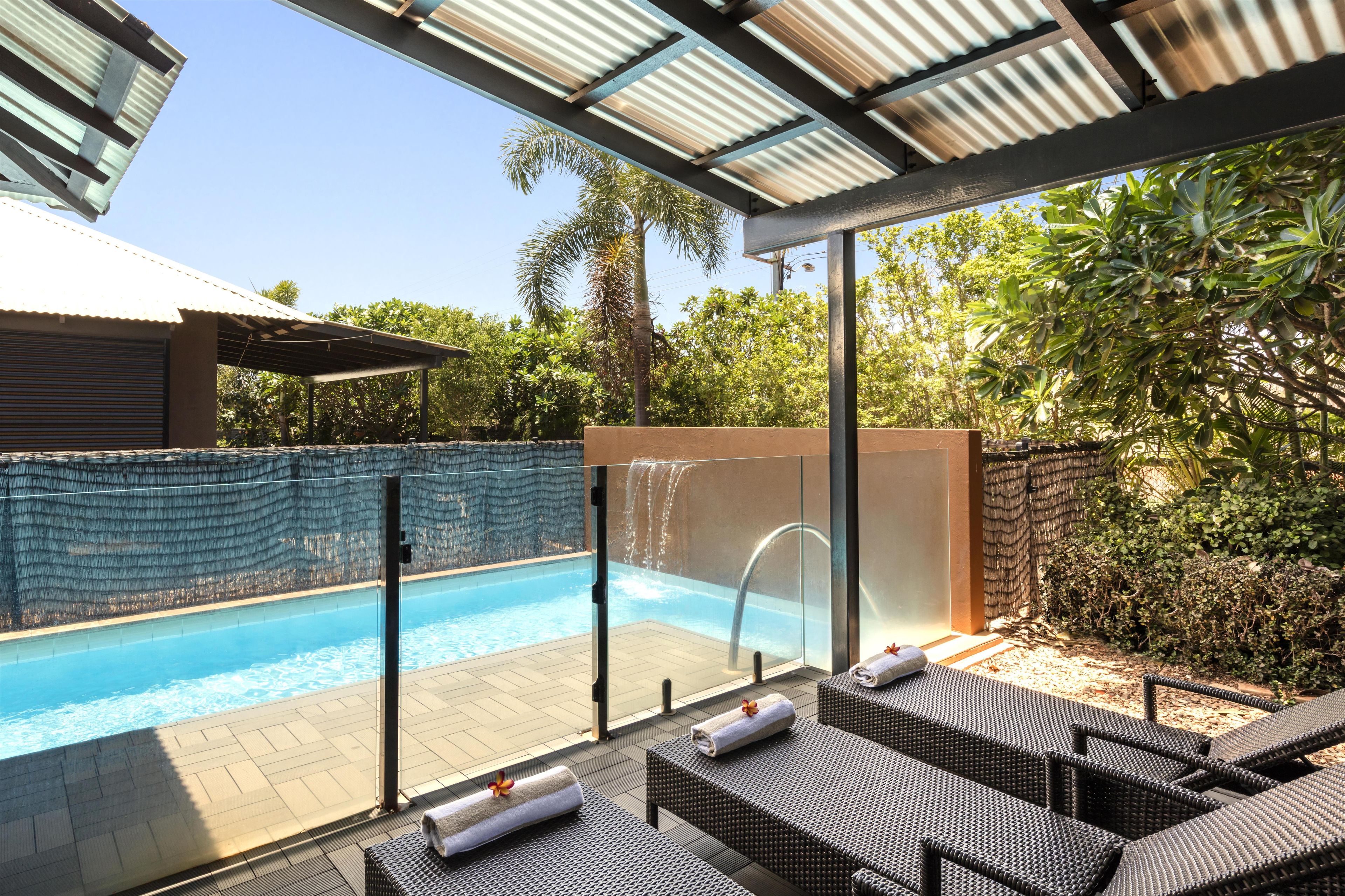 A poolside area with lounge chairs, a glass-enclosed pool, and a waterfall feature.