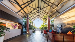 A covered outdoor area with a reception desk, wooden benches, and potted plants.