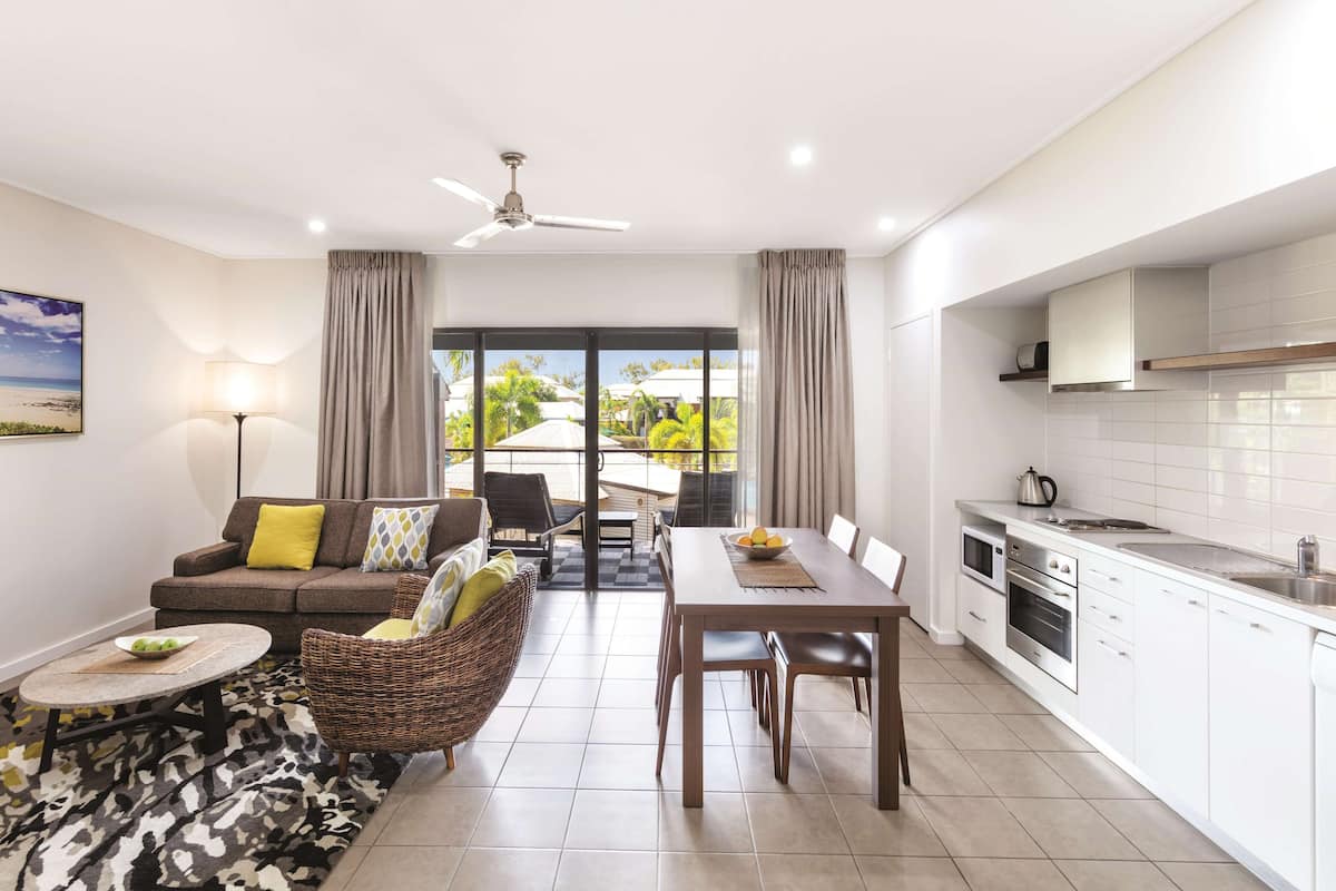 A modern living room with a sofa, dining table, and kitchen area with white cabinets and appliances.