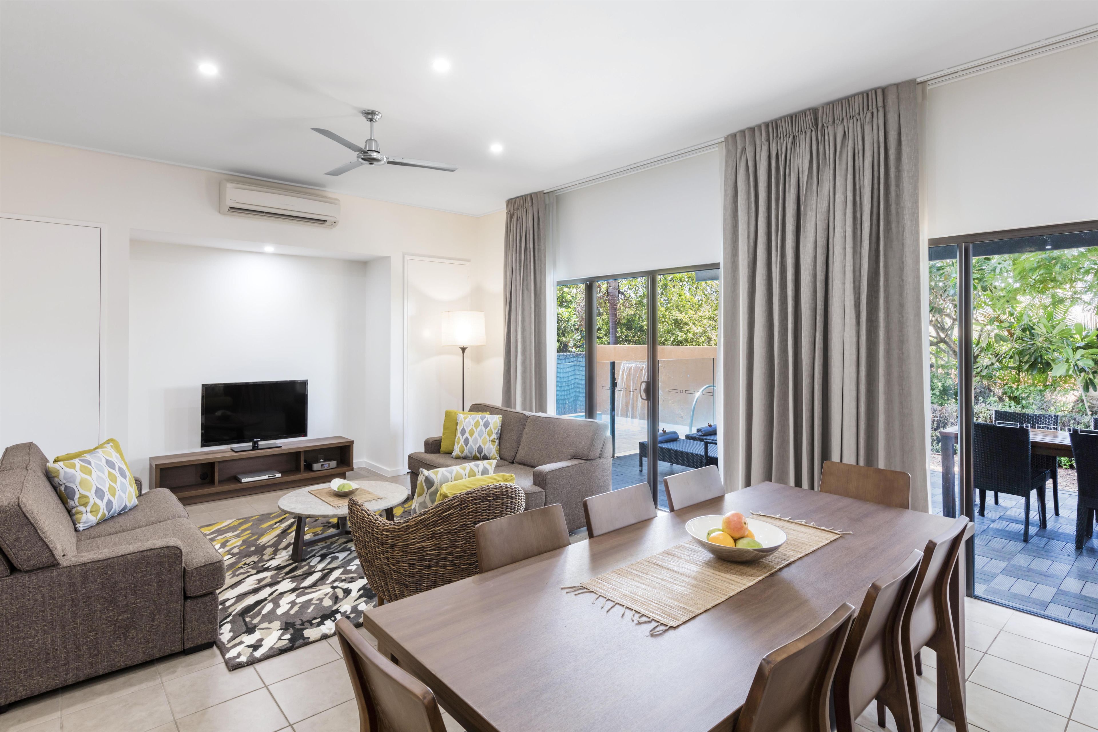 A modern living room with a flat-screen TV, sofa, and dining area with a view of the outdoors.