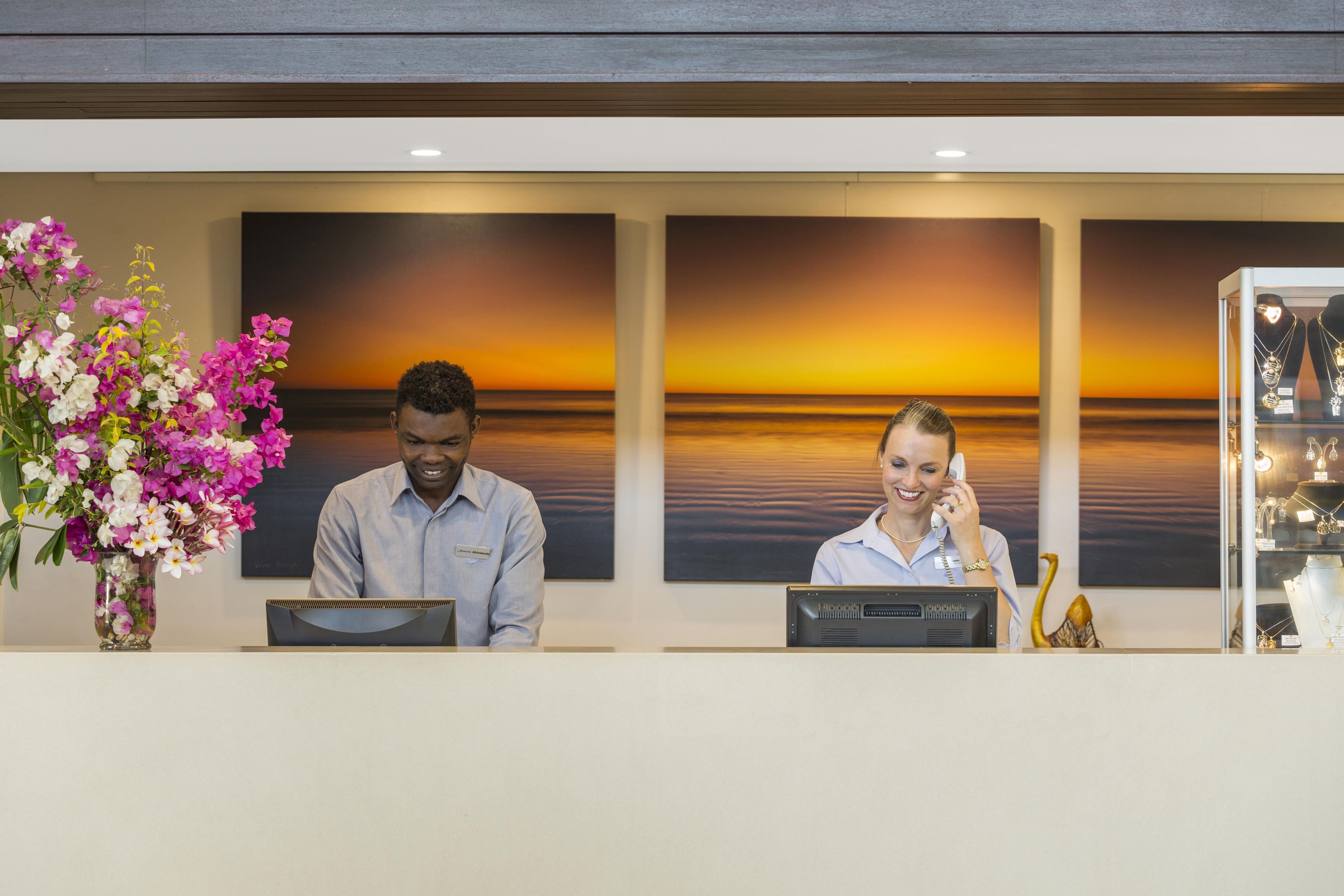 A reception desk with two staff members, a vase of flowers, and a display of jewelry.