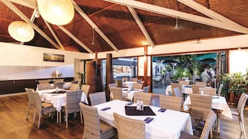 A restaurant with high ceilings, wicker furniture, and a view of the outdoor area.
