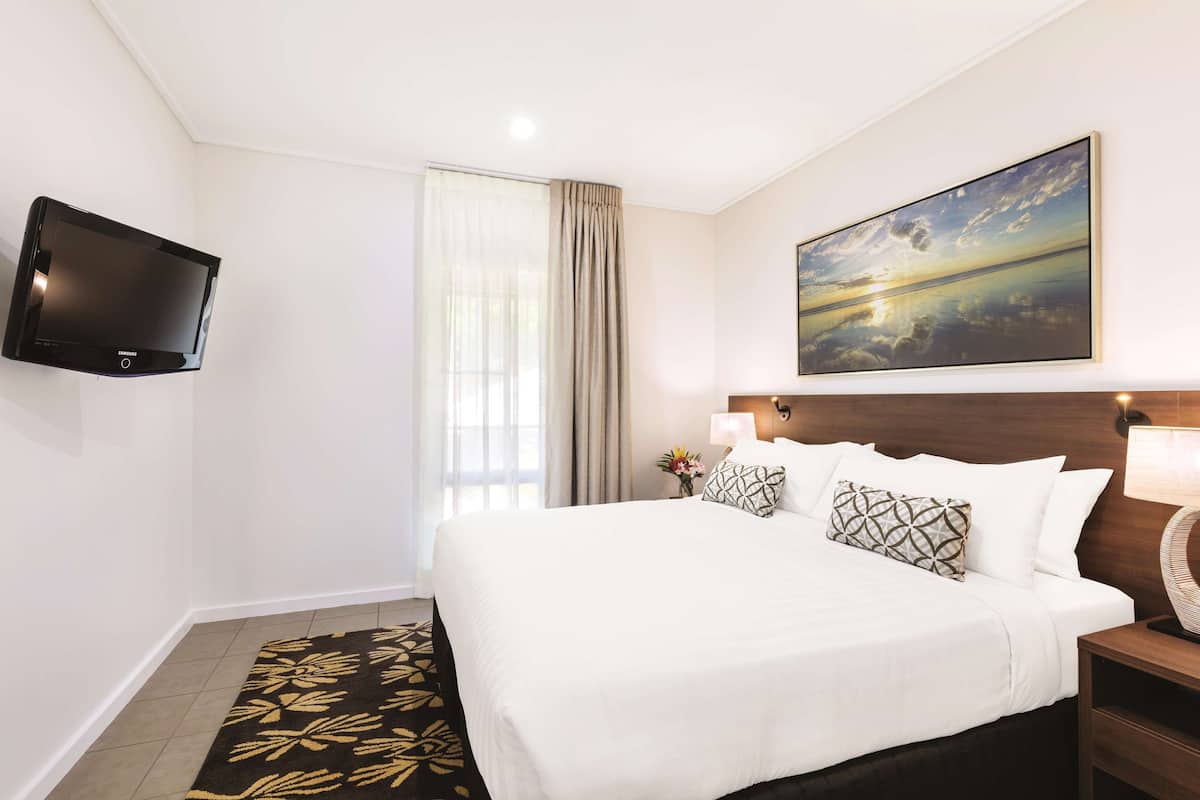 A hotel room with a bed, a flat-screen TV, a painting, a nightstand, and a window with curtains.