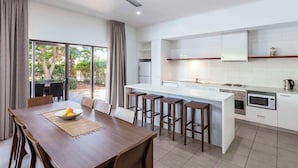 A modern kitchen with a central island, bar stools, and a dining area with a table and chairs.