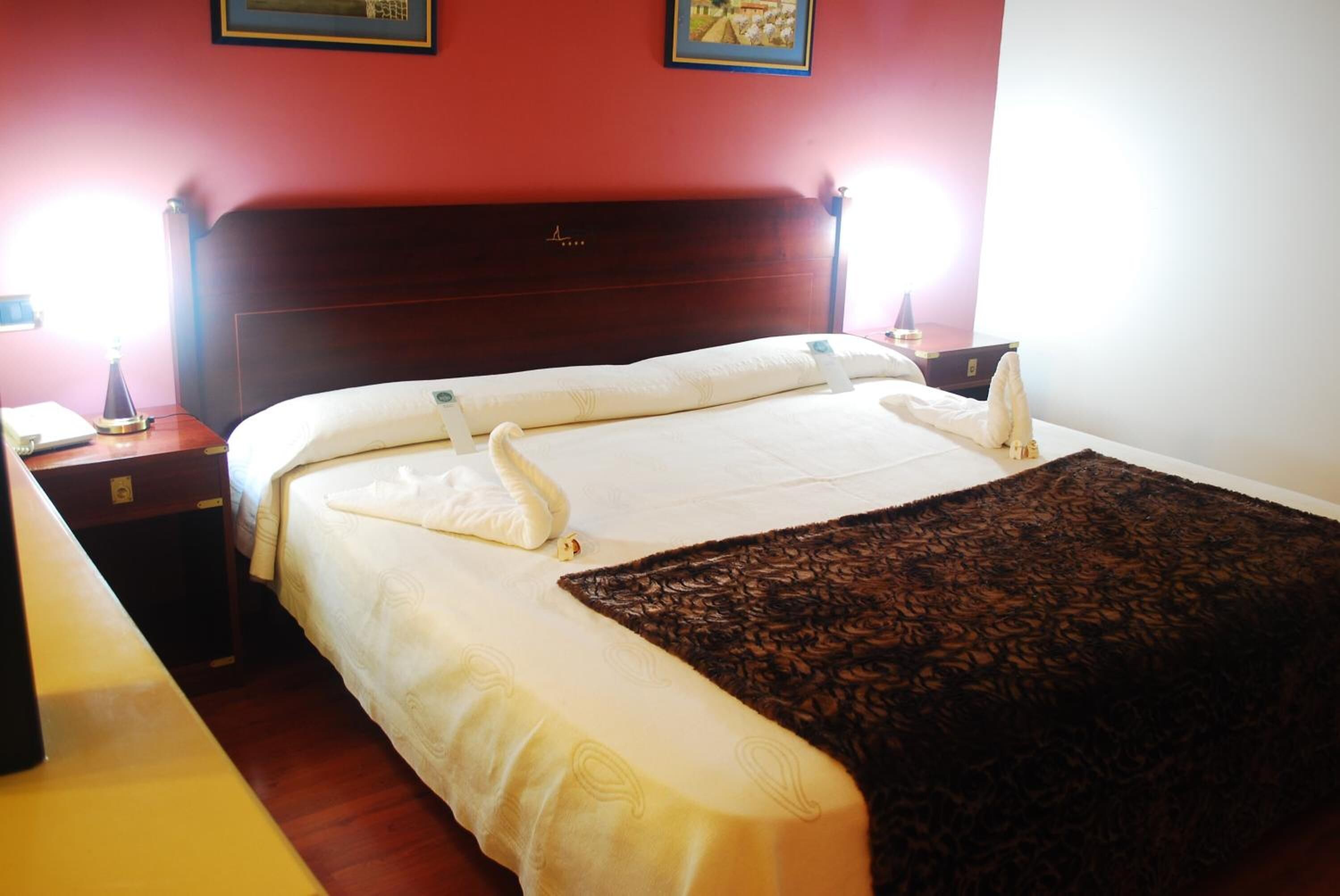 A hotel room with a wooden headboard, a bed with white bedding, a brown throw blanket, and bedside lamps.