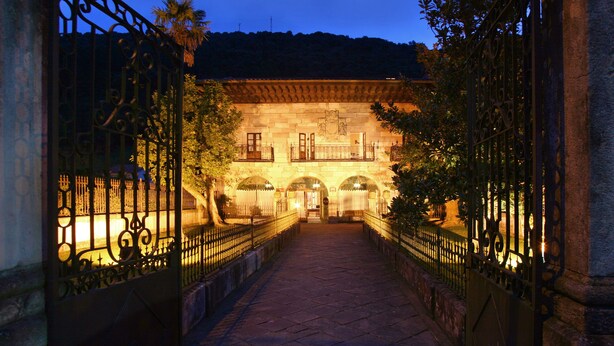 A stone building with arched doorways and balconies, surrounded by wrought iron gates and a cobblestone pathway. - Palacio Guevara (Valdaliga)