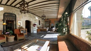 A spacious lobby with stone walls, wicker furniture, and a large window overlooking a garden. - Palacio Guevara (Valdaliga)