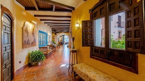 A corridor with wooden beams, tiled flooring, a bench, and a window with a view of buildings outside. - Hospedium Hotel Retiro del Maestre (Almagro)