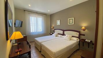 A hotel room with two beds, a desk with a lamp, a TV, and two bedside lamps.