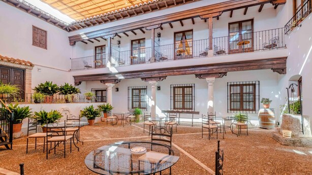 A spacious courtyard with a central glass table surrounded by chairs, potted plants, and outdoor seating areas. - Hospedium Hotel Retiro del Maestre (Almagro)
