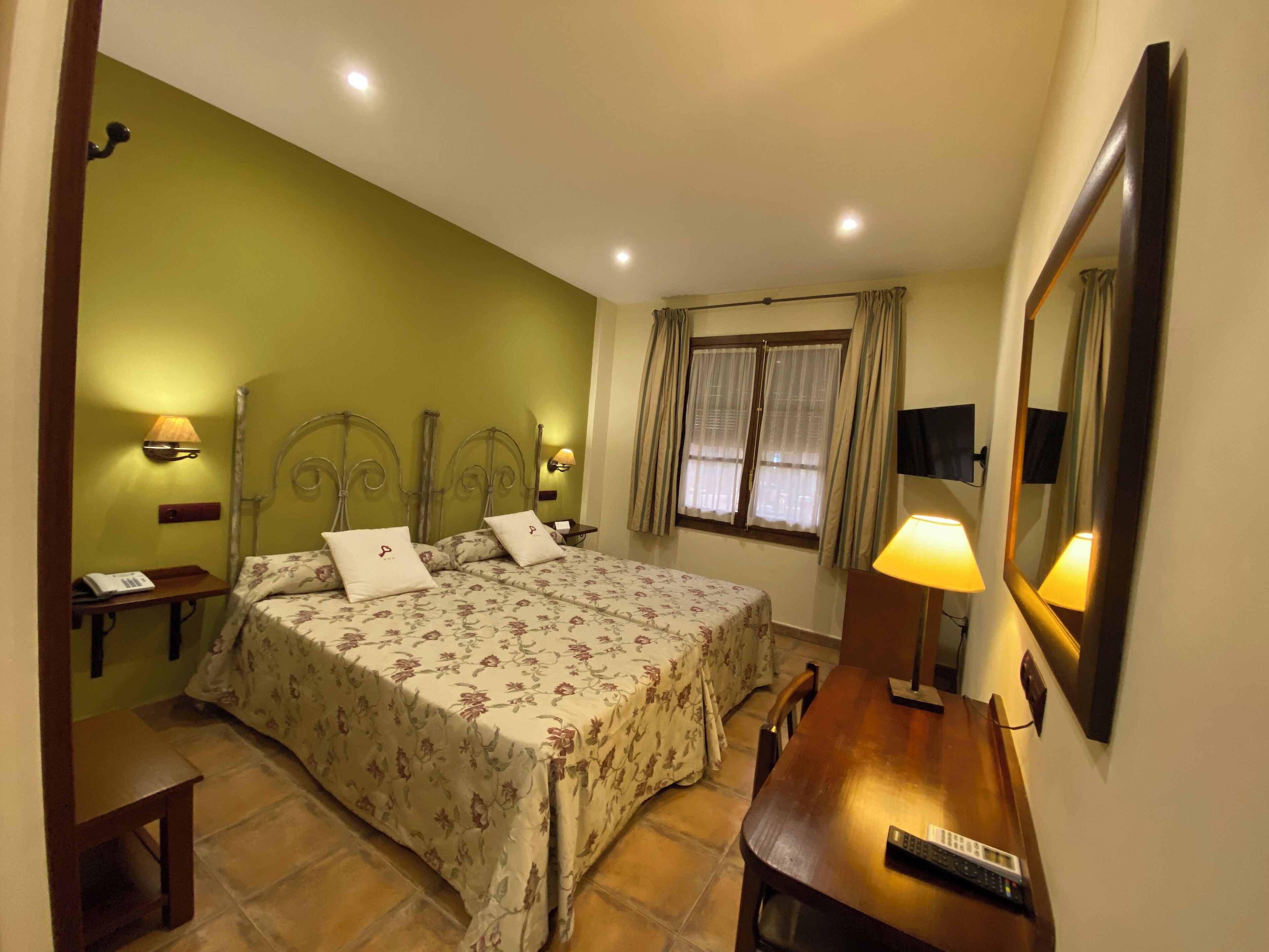 A bedroom with a bed, bedside tables, a mirror, a window with curtains, and a television.