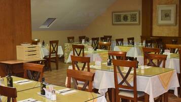 Un espace repas comprenant plusieurs tables et chaises, dont certaines sont dotées de plateaux en verre et recouvertes de nappes blanches.