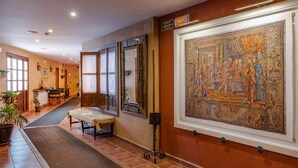 A hotel corridor with a large mural on the wall, a bench, and a reception area in the distance. - Hospedium Hotel Retiro del Maestre (Almagro)