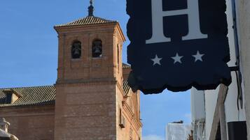 Una calle estrecha con un edificio histórico que presenta una torre de campanas y un letrero con una 'H' grande y estrellas.