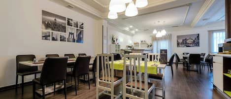 A hotel dining area with multiple tables and chairs, a reception desk, and wall-mounted artwork.