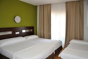 Habitación de hotel con dos camas, una pared verde y una ventana con cortinas.