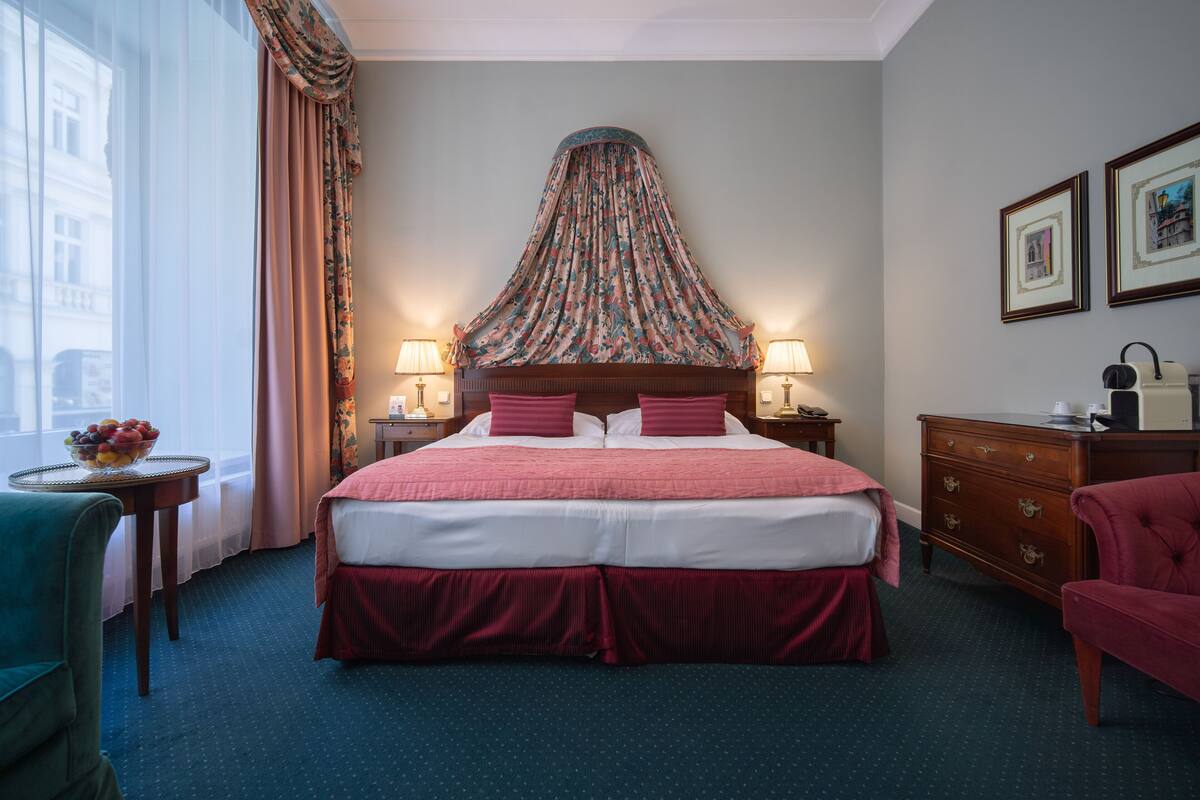 A hotel room with a large bed, a nightstand with a lamp, a dresser, and a chair.