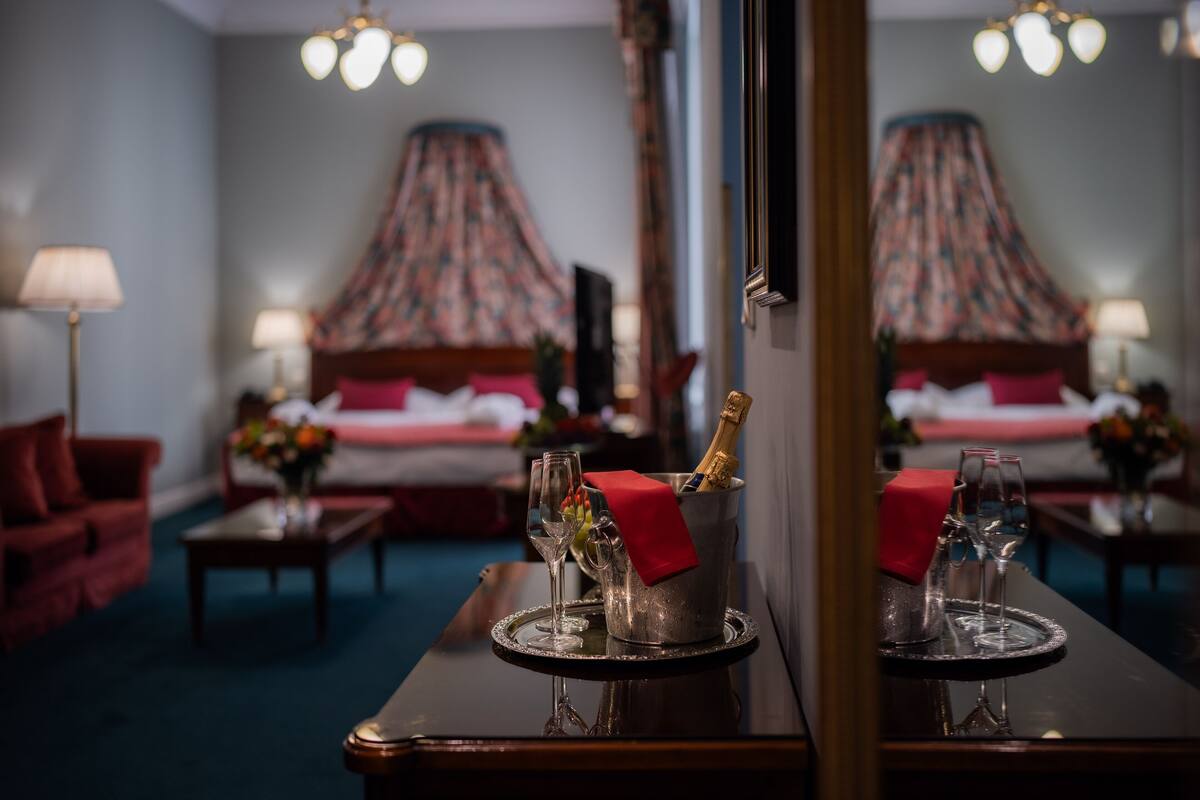A hotel room with a bed, a bedside table with a bottle of champagne, and two glasses.