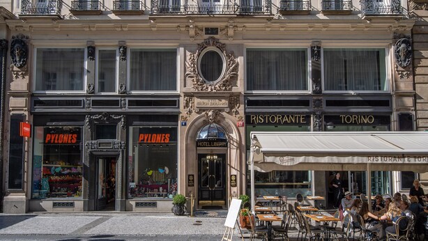 A hotel facade with flags, a central entrance, and storefronts for 'Pylons' and 'Ristorante Torino'. - Hotel Liberty (Prague)