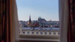 A view of a cityscape through a window, featuring a prominent church spire and a large historic building. - Hotel Liberty (Prague)