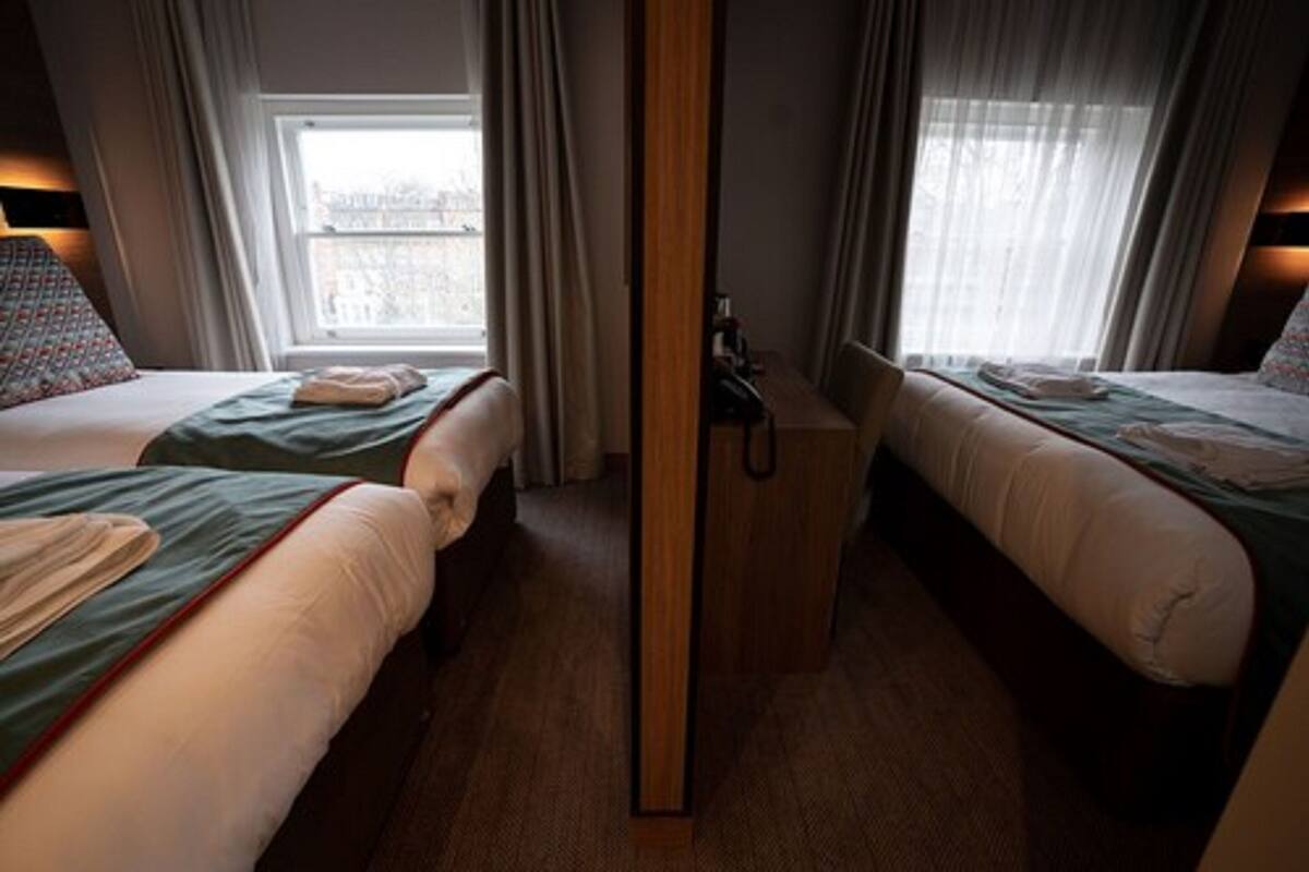 A hotel room with two beds, a wooden wardrobe, and a window with curtains.