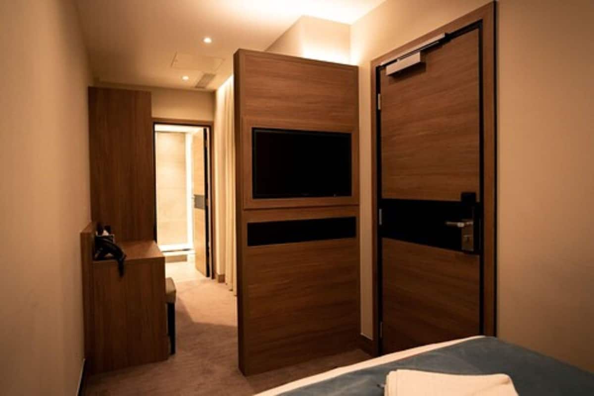 A bedroom with a bed, a TV mounted on the wall, and a wooden wardrobe.